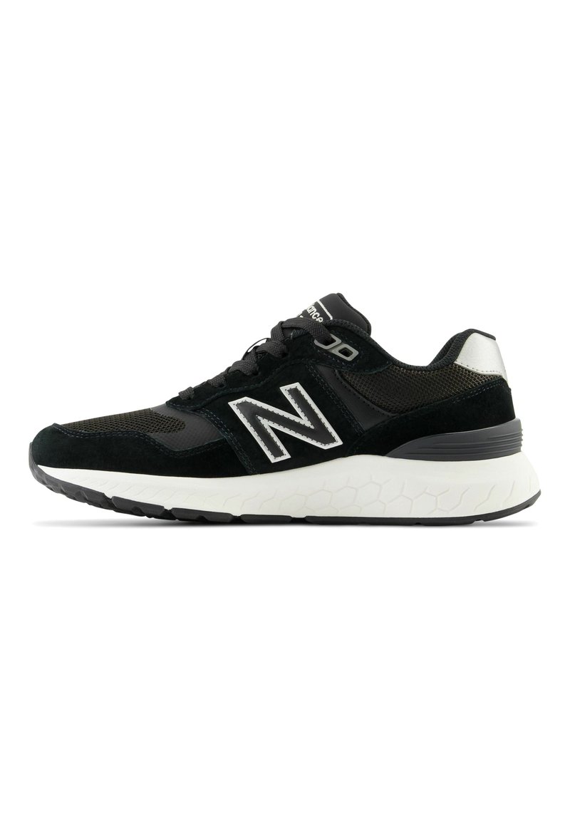 Chaussures de sport noires avec un dessus en maille et en daim, présentant un logo blanc et une semelle intermédiaire texturée blanche avec une semelle extérieure en caoutchouc noir.