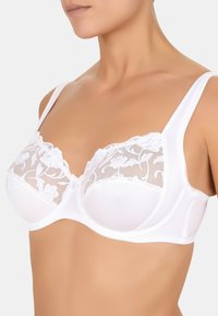 Biały stanik z przezroczystą koronką w kwiatowe wzory na miseczkach, gładkimi materiałowymi ramiączkami oraz balkonowym kształtem dla lepszego wsparcia.