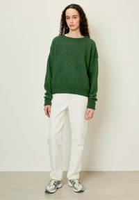 Maglione verde a maglia con una vestibilità ampia, polsini e scollo a coste. Abbinato a jeans bianchi a gamba dritta e scarpe da ginnastica multicolori.