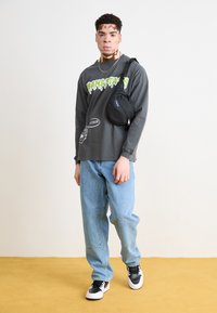 Gray long-sleeve shirt with green graphic text, light blue baggy jeans, and black sneakers with white soles. Small black crossbody bag.