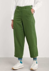 Gröna vida byxor i solid bomull, med knäppning, bältesöglor och fickor. Bärs med vita sneakers och randiga strumpor.