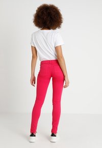 Figurbetonte rosa Jeans mit glatter Textur und Fünf-Taschen-Design. Kombiniert mit einem schlichten weißen T-Shirt und weißen Sneakern.