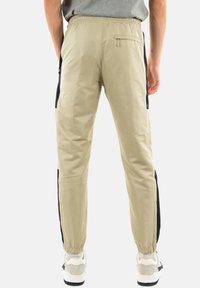 Pantalones cargo beige con una textura suave, cinturilla elástica, paneles laterales negros y detalles de bolsillo con cremallera. Combinados con zapatillas blancas.