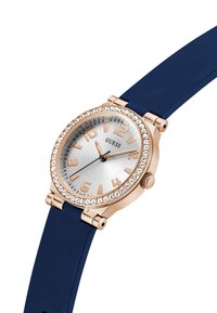 Roosa kuldne kell hõbedase kelladialiga, tumesinine silikoonist rihm ja selged kristallaktsendid bezelil. Omab julgeid tundemarke.