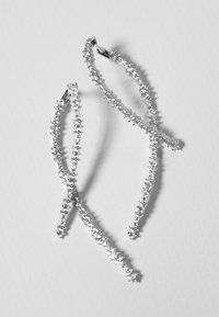 Orecchini in argento con un design allungato e curvo adornato da scintillanti cristalli trasparenti, che presentano una finitura testurizzata e luccicante.