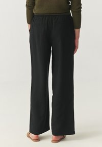 Zwarte wijde broek met een elastische tailleband en twee achterzakken. Gemaakt van een lichtgewicht stof met een gladde textuur.