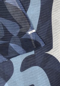 Tissu plissé à motif bleu foncé et bleu clair avec une petite étiquette blanche portant l'inscription "CECIL" cousue près du centre.