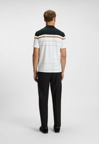 T-shirt med kort ärm, vit bas, svarta axlar och horisontella ränder i beige, omgivna av svart. Bärs med svarta byxor.