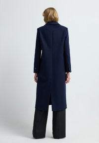 Marineblaue Wolljacke mit geradem Schnitt, langen Ärmeln und Einknopfbündchen. Verfügt über einen Schlitz in der Mitte des Rückens und ein minimalistisches Design.
