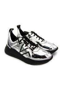 Silberne metallische Sneaker mit schwarzen Akzenten, die eine dicke Sohle, Netzpaneele und ausgeprägte Ösen für die Schnürsenkel aufweisen. Auffälliges dreieckiges Design.