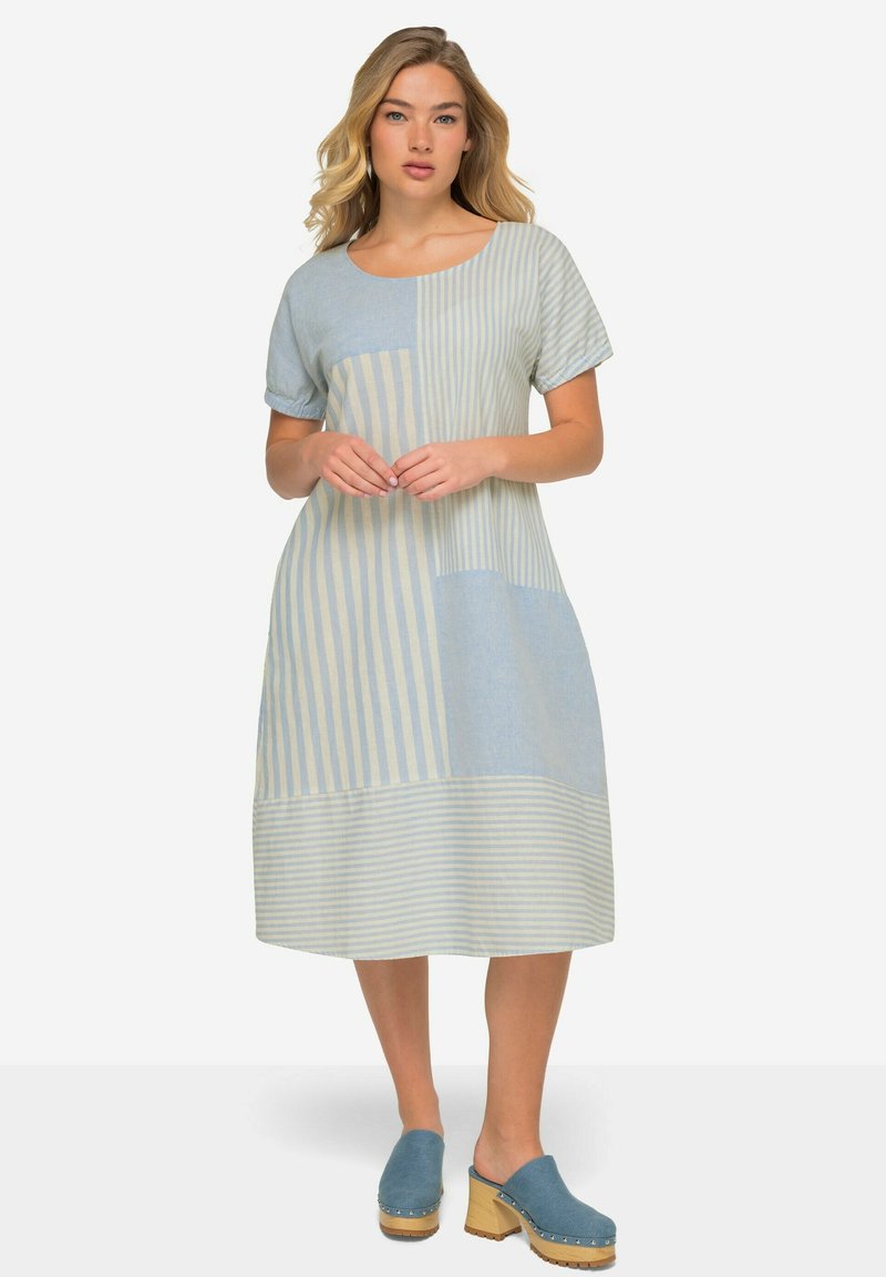 El vestido de color azul claro, de longitud hasta la rodilla, presenta una mezcla de patrones sólidos y rayados, con mangas cortas y un escote redondo. Combinado con zuecos azules.