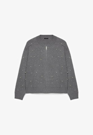 Grå strikket cardigan med lynlåslukning, der har teksturerede polkaprikkede detaljer. Ribstrikket kant og ærmeafslutninger for ekstra detalje.