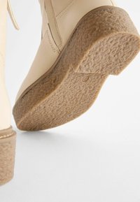 Cremefarbene Knöchelstiefel mit einer strukturierten Gummisohle, einem glatten Lederoberteil und einer genähten Nahtdetails. Der Absatz hat ein niedriges, klobiges Design.