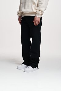 Pantalons en denim noir à coupe ample, assortis à un sweat à capuche couleur crème avec une poche avant. Complétés par des baskets blanches.