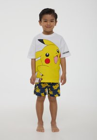 T-shirt bianca con grande grafica di Pikachu gialla; pantaloni corti blu navy con motivo ripetuto di Pikachu; vestibilità casual, maniche corte.