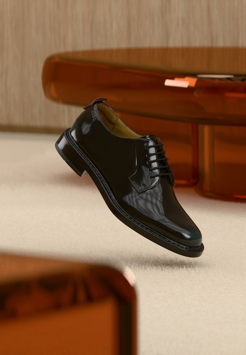 Μαύρο γυαλιστερό δερμάτινο επίσημο παπούτσι με κορδόνια αιωρείται πάνω από μια μπεζ μοκέτα, με θολά καφέ έπιπλα στο φόντο.