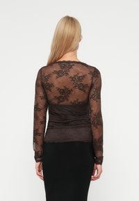 Zwarte kant lange mouw top met bloemenpatronen, een aansluitend ontwerp en gerimpelde details bij de taille. Doorzichtig materiaal met gegolfde randen.