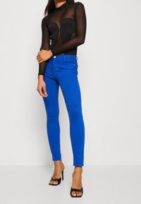 Top negro de mangas largas con detalles recortados combinado con jeans ajustados azul brillante y sandalias de tacón alto negras, resaltando un look ceñido.