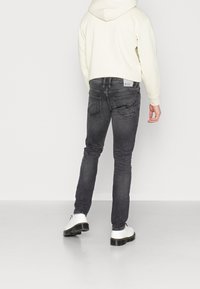 Mörkgrå denimjeans med tight passform, bakfickor och en etikett märkt "DENIM." Bärs med en vit huvtröja och vita skor.