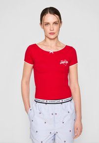 Rød kortermet topp med rund hals, med hvit kant og en liten sløyfedetalj; inkluderer 'tommy girl' logo nær brystet.