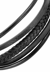 Corde intrecciate e lisce in pelle nera disposte a strati, che mostrano una cucitura testurizzata lungo la sezione intrecciata.