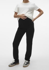 Svarta stretchbyxor med hög midja, kombinerat med en vit t-shirt med kort ärm och svarta sneakers med grå detaljer.