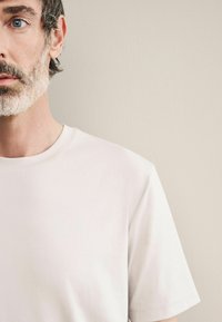 Jasno beżowa koszulka z krótkim rękawem, wykonana z gładkiego materiału, z okrągłym dekoltem i minimalistycznym wzornictwem.