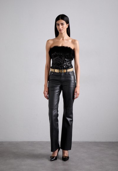 Μαύρη κορυφή χωρίς τιράντες με παγιέτες και φτερά, συνδυασμένη με μαύρο δερμάτινο παντελόνι ψηλής μέσης και μυτερές μαύρες γόβες με χρυσές λεπτομέρειες.