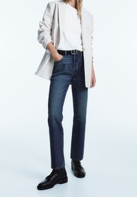 Jeans i mörkblått denim, rak passform, kombinerat med en vit t-shirt och en beige blazer. Svarta snörstövlar fulländar outfiten.