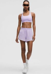 Ljuslila sportbh och matchande shorts i glatt tyg, bärs med vita sneakers och strumpor, samt svarta solglasögon.