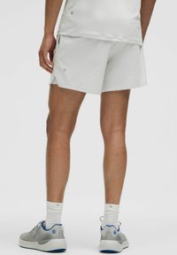 Pantalones cortos deportivos blancos con un ajuste holgado, que cuentan con aberturas laterales y una sutil marca. Combinados con zapatillas grises y calcetines blancos de tobillo.