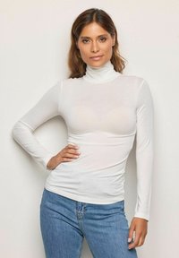 Biały, długi rękaw, golfowy top wykonany z cienkiego, lekkiego materiału, w połączeniu z jeansami w kolorze niebieskim, o wysokim stanie. Gładka tekstura, dopasowany krój.