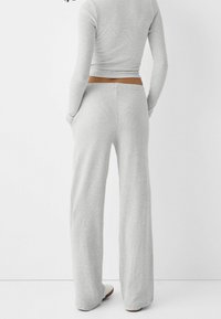 Set a due pezzi di un leggero grigio chiaro, con top a maniche lunghe cropped e pantaloni ampi con una vita marrone, caratterizzato da una texture liscia.