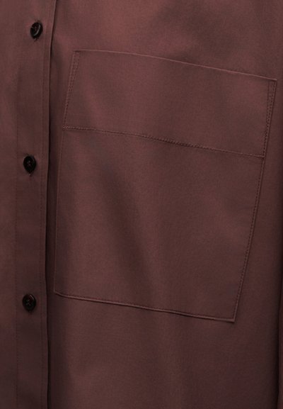 Chemise marron avec une grande poche rectangulaire sur la poitrine et des boutons noirs le long de la pate de boutonnage avant.