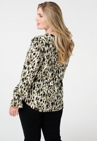 Blouse à manches longues en crème avec un imprimé animal noir et or, présentant une finition texturée et des manches gathers. Associée à un pantalon sombre.