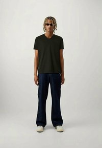 Μαύρη βαμβακερή μπλούζα v-neck συνδυασμένη με αέρινα σκούρα τζιν και λευκά sneakers. Το μοντέλο φορά γυαλιά ηλίου και έχει τα μαλλιά πλεγμένα.