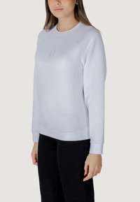 Sudadera azul claro con puños y dobladillo acanalados, que presenta un sutil logo en relieve en el pecho. Textura de tela suave y lisa.