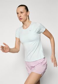 Heleheline sportlik särk lühikeste varrukatega ja ümmarguse kaelusega, millel on väikesed perforatsioonid; koos roosa lühikesed pükstega.