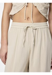 Ljust beige, vida byxor med elastisk midja och snöre. Strukturerad tyg med subtila veck.