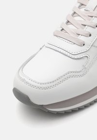 White leather sneaker with light grey accents, textured stitching, subtle curves, and a grey rubber sole. Lace closure with light tan laces.