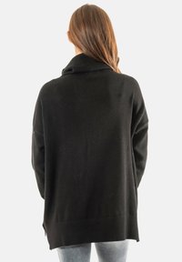 Suéter negro oversized con un cuello de tortuga acanalado, hombros caídos y aberturas laterales, confeccionado en una tela suave con una textura lisa.