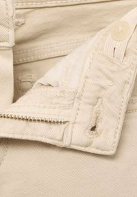 Beige puuvillakangas, jossa on lähikuva vetoketjusta ja nappisulkeista. Ominaisuuksiin kuuluu kulunut yksityiskohta ja sileä, tekstuurinen pinta.