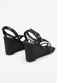 Las sandalias de cuña negras presentan múltiples correas cruzadas, una correa ajustable en el tobillo con hebilla, y un tacón de cuña texturizado.
