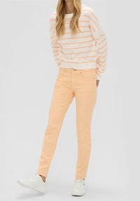 Hellrosa gestreifter Pullover mit weitem Ausschnitt, kombiniert mit pastelloranfarbenen Skinny Jeans und weißen Sneakers. Glatte Textur und klassischer Schnitt.