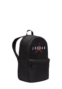 Mochila negra con parte superior redondeada, que cuenta con un bolsillo frontal con cremallera, un gran logo "JORDAN" y un acento rojo sobre una superficie de tejido suave.