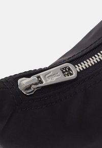 Borsa in tessuto blu navy con cerniera argento e un'etichetta con il logo, caratterizzata da cuciture testurizzate e una finitura liscia.