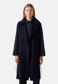 Navy blue wool long coat with a wide collar, open front, and side pockets. The sleeves are wide and the texture appears soft.