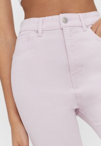 Jean en denim rose clair avec une coupe ajustée, un style à cinq poches, une fermeture par bouton métallique et des détails de couture subtils.