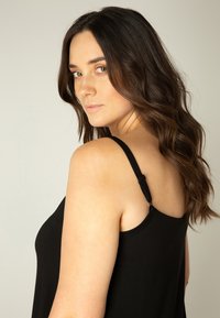 Zwarte tanktop met dunne sp straps, voorzien van verstelbare hardware. Zachte stof met een gladde textuur, gedragen door een model met golvend haar.