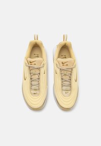 Nike Air kingad heledas kollases võrkkangas, millel on kumerad kujundid. Omavad kuldset brändimist ja aktsente, beeži paelu ning valget kummist tallat.